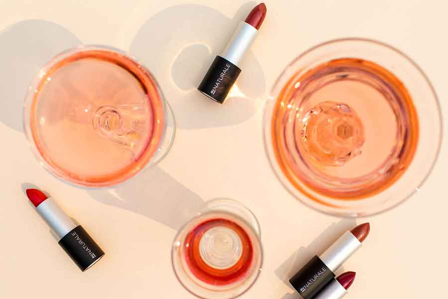 AuNatural Liptstick displayed on a peach colored paper next to some glasses of rose colored drinks
