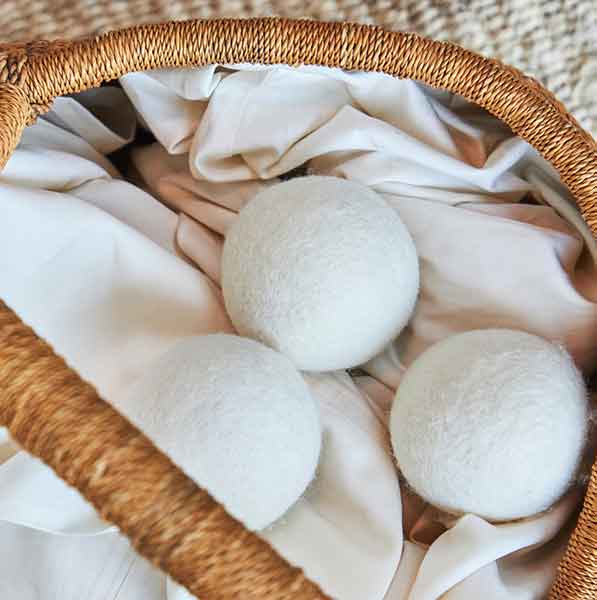 3 wool dryer balls in a basket filled sheets on top of carpet