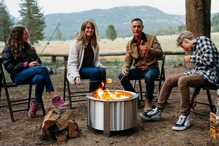 Stainless Steel Firepit with 4 people sitting on chairs outdoors in the background