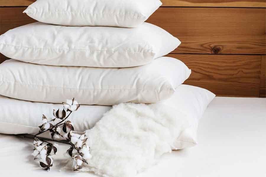 4 white pillows stacked by size on white surface with wooden background
