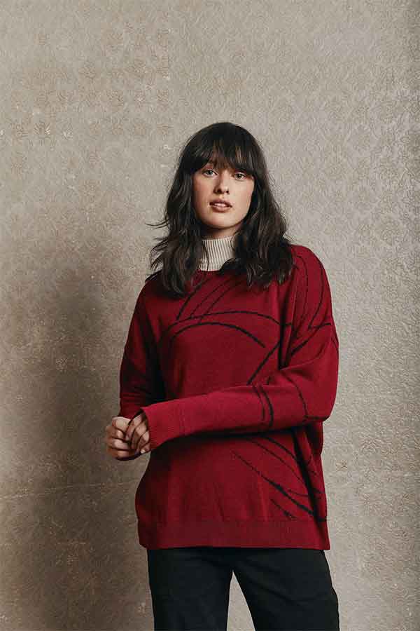 Woman wearing a red sweater and black pants in front of a grey background