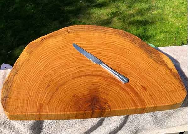 Image of cutting board made of a tree with knife on top and grass in the background