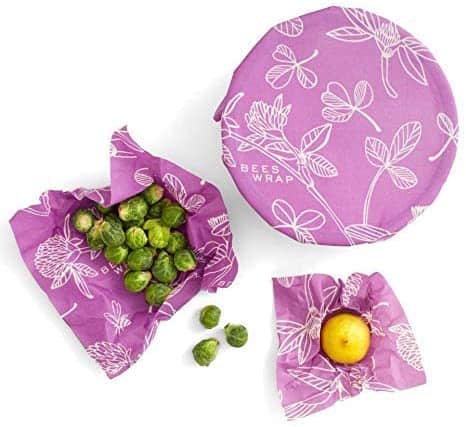 Bee's Food Wrap in a Purple Floral Pattern wrapped on a bowl and two other wrapping brussel sprouts and the other a lemon.