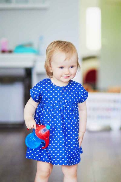 Baby girl holding blue and red sippy cup inside a house
