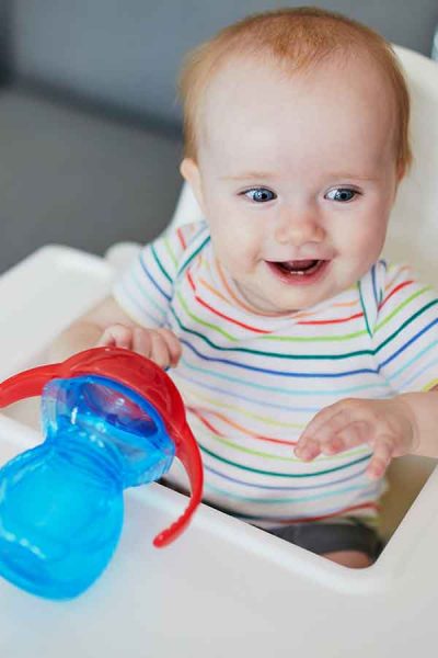 Baby smiling in white high chair with blue and red sippy cup