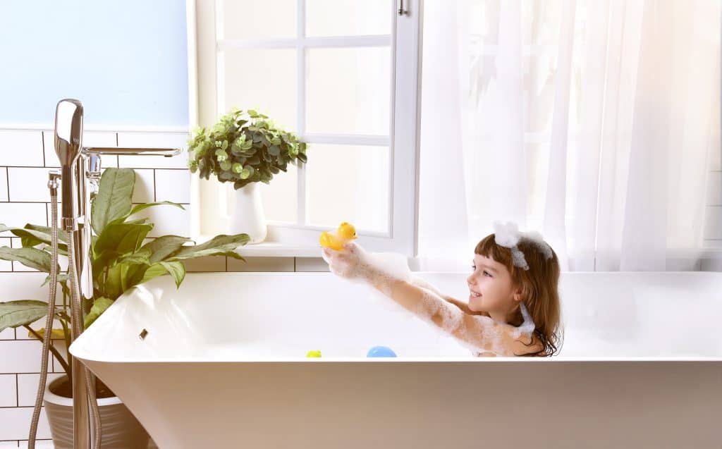 Happy little girl sitting in bath tub in the bathroom playing with non-toxic bath toys