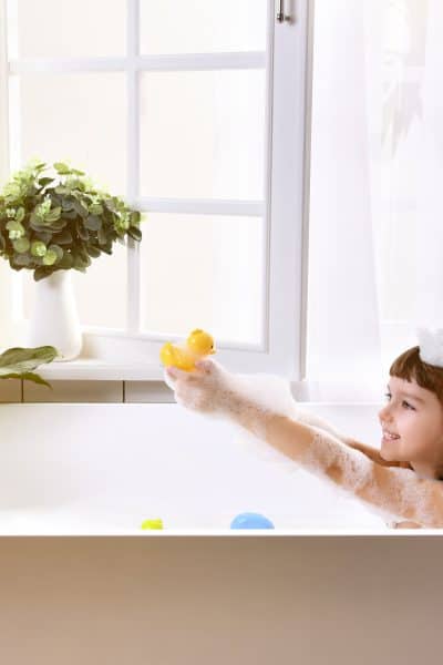 Happy little girl sitting in bath tub in the bathroom playing with non-toxic bath toys