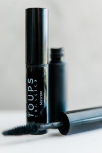 Image of mascara brush and mascara container on white surface