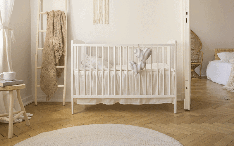 white crib with white organic crib sheets and hearts hanging from outside of crib