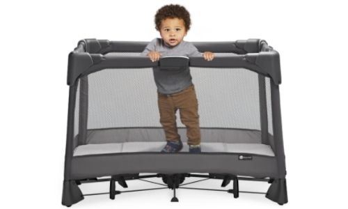 boy standing inside of grey travel crib