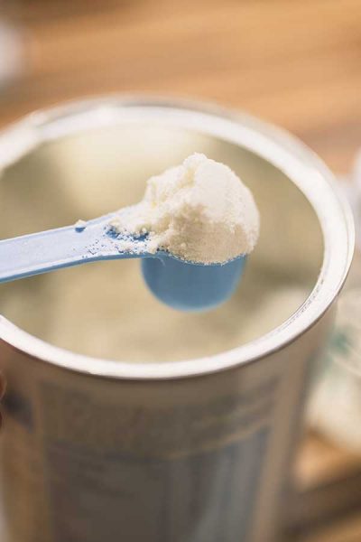 Powder milk for baby and blue spoon on light background close-up. Milk powder for baby in measuring spoon on can. Powdered milk with spoon for baby. Baby Milk Formula and Baby Bottles. Baby milk formula on kitchen background