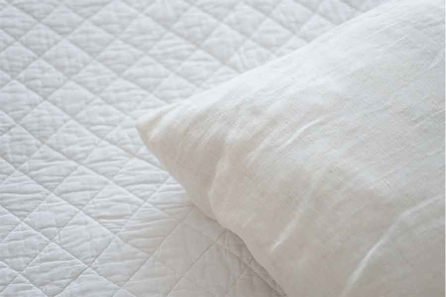 A white pillow on a white quilted sheet