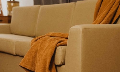 tan organic couch with orange blanket draped over back and front