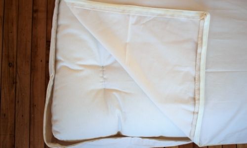 unzipped corner of a white organic waterproof mattress protector on a bed
