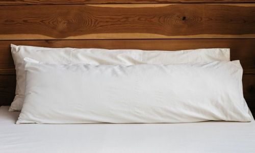two white organic body pillows on a bed with white sheets 