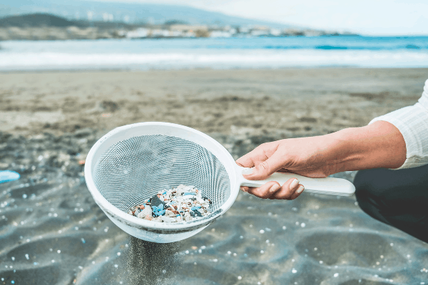 woman holding mesh strainer at the beach filled with sea glass and plastic 