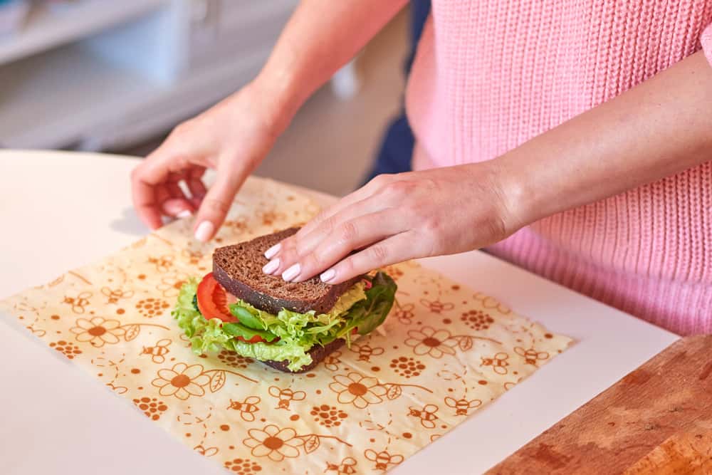 Woman hands wrapping a healthy sandwich in beeswax reusable food wrap. 