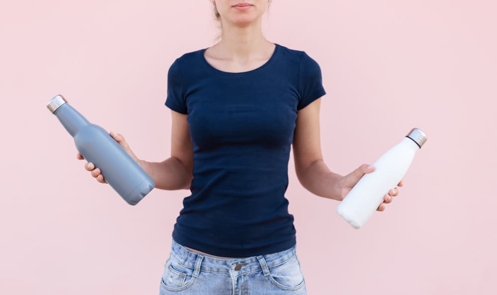 Woman holding two eco-friendly water bottles - steel thermo water bottles, white and grey in color.