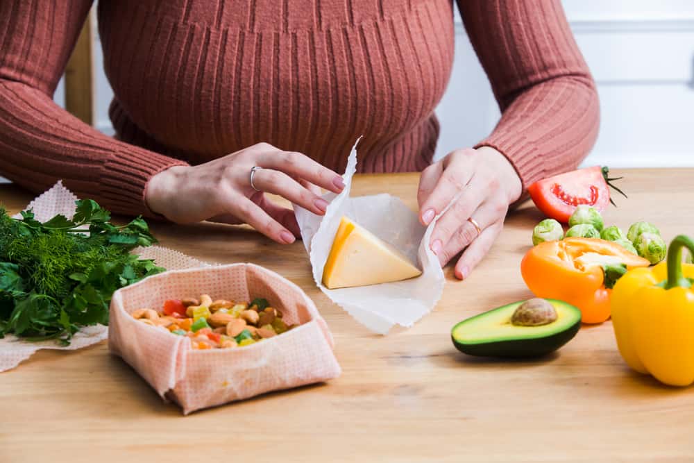 Woman using ecological reusable wrapping for healthy and fresh food storage while wrapping her cheese, nuts, and vegetables