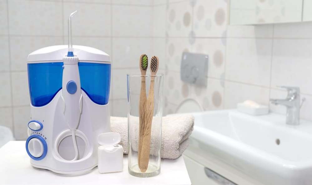 Natural Dental Flosses - Tools for cleaning teeth in the bathroom. Waterpik and dental floss with bamboo eco toothbrushes sitting near white bathroom sink. Zero waste, sustainable bathroom and lifestyle.