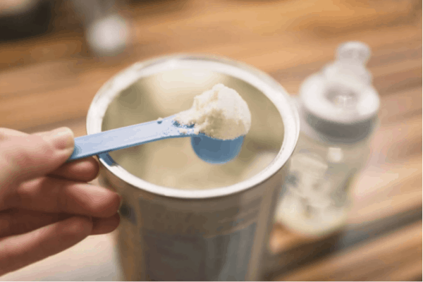 scooping organic formula from a tin can with a blue measuring scoop.  