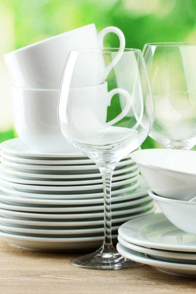 Picture of stacked white dishes, bowls, and clear wine glasses with green background