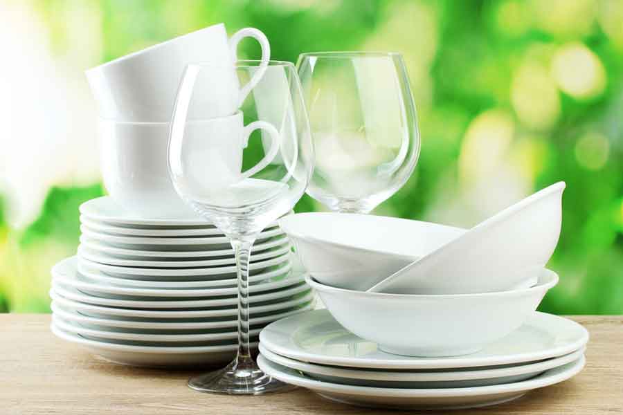 Picture of stacked white dishes, bowls, and clear wine glasses with green background