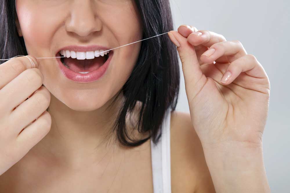 Woman flossing her teeth - Natural Dental Flosses