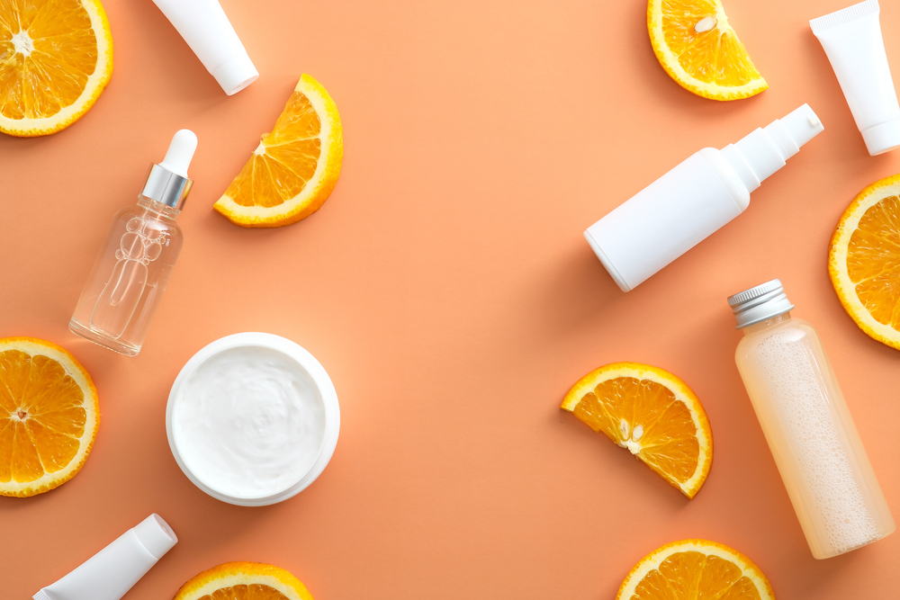 Natural cosmetic with Vitamin C. White bottles mockups, jar of moisturizer, sliced orange top view.