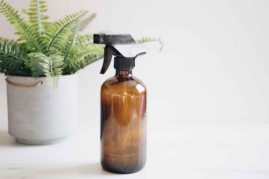 Brown plastic spray bottle on a white table with a potted plant in the background
