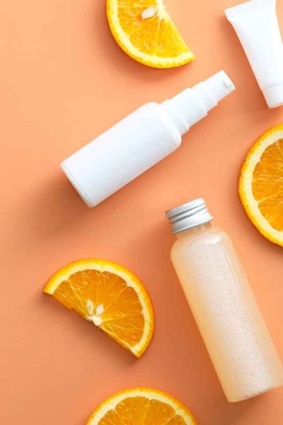 Natural cosmetic with Vitamin C. White bottles mockups, jar of moisturizer, sliced orange top view. Vitamin C Featured Image