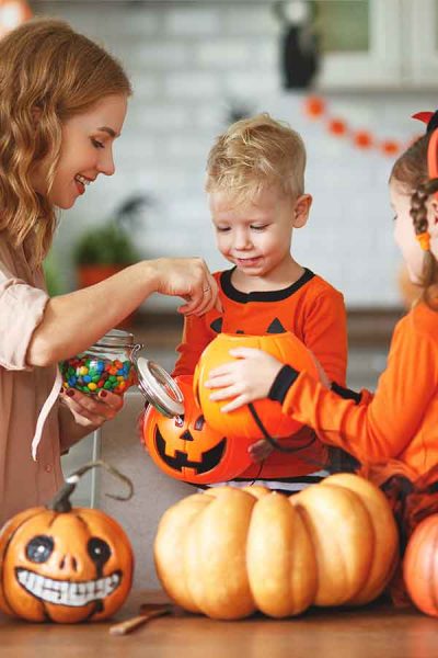 A mother giving candy and celebrating Halloween with her 2 kids